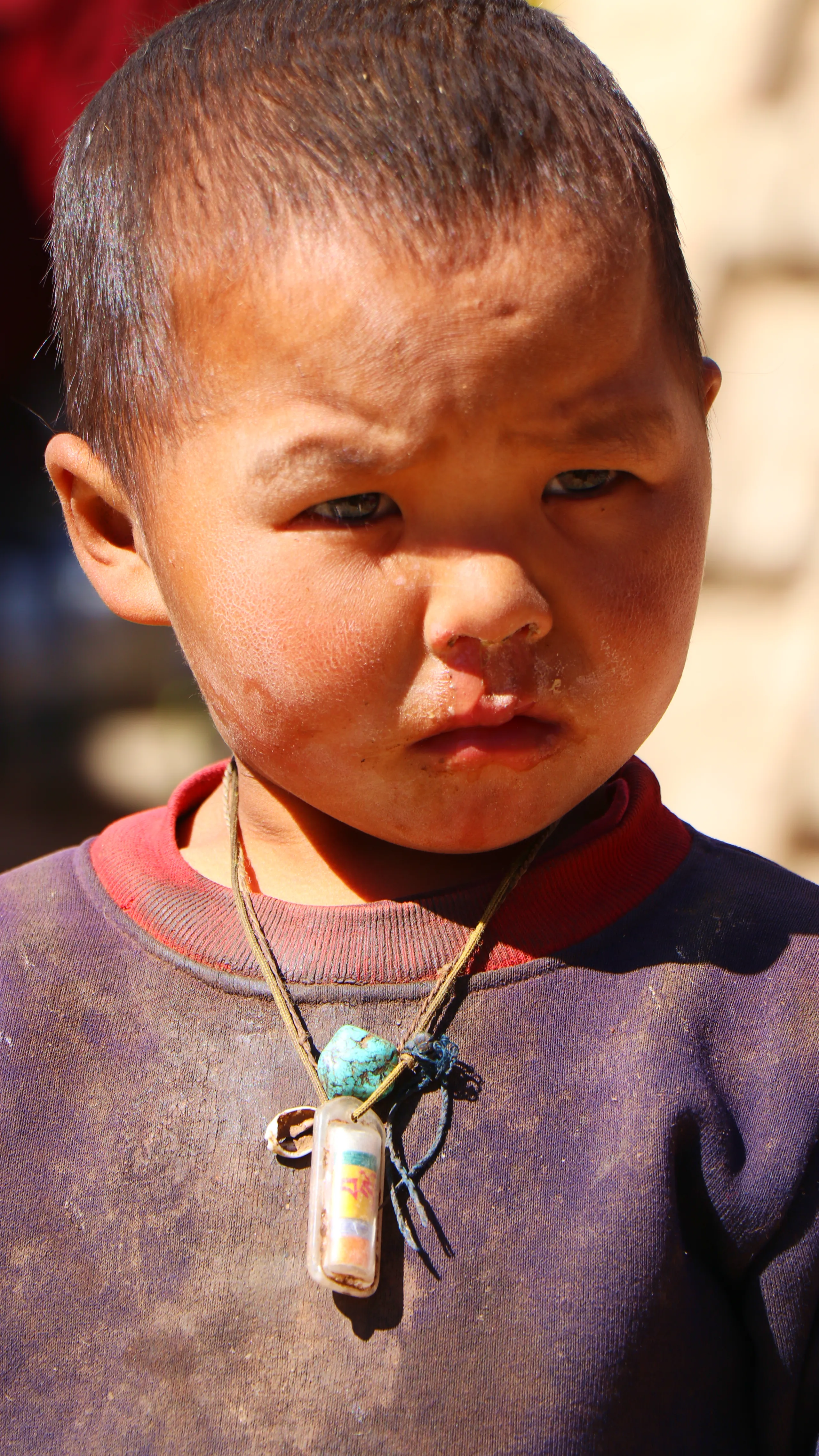 A close-up portrait of a very young child, approximately 2-3 years old, with short dark hair and East Asian features. The child has a furrowed brow, wide dark eyes, and a slightly pursed, pouty expression - looking directly at the camera with an expressio