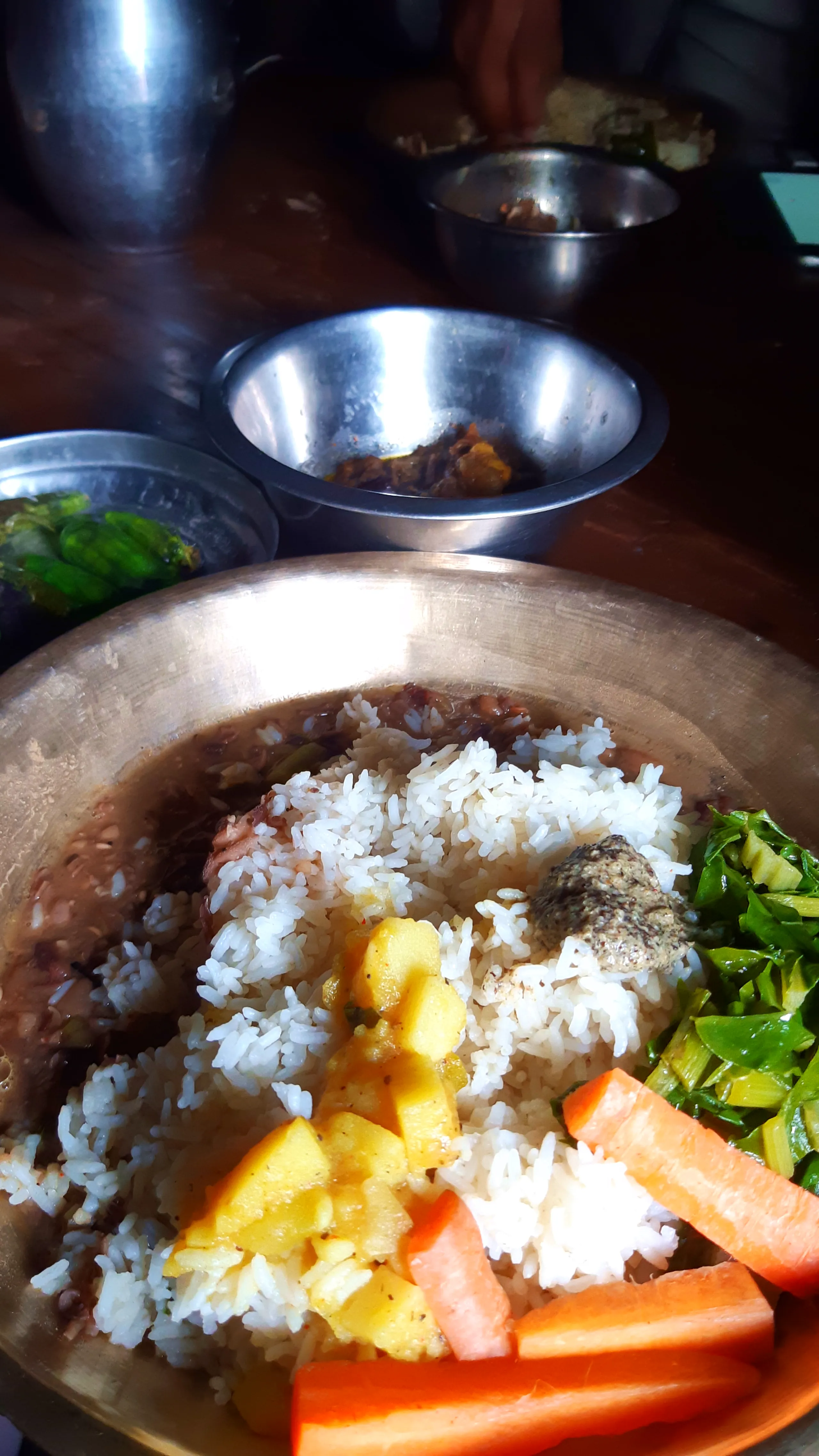 A close-up of a traditional Nepali Dal Bhat meal, served on a large, round copper-bronze thali plate. The plate is generously loaded: a tall mound of white rice sits in the center, topped with a yellow potato curry (with visible potato chunks and turmeric