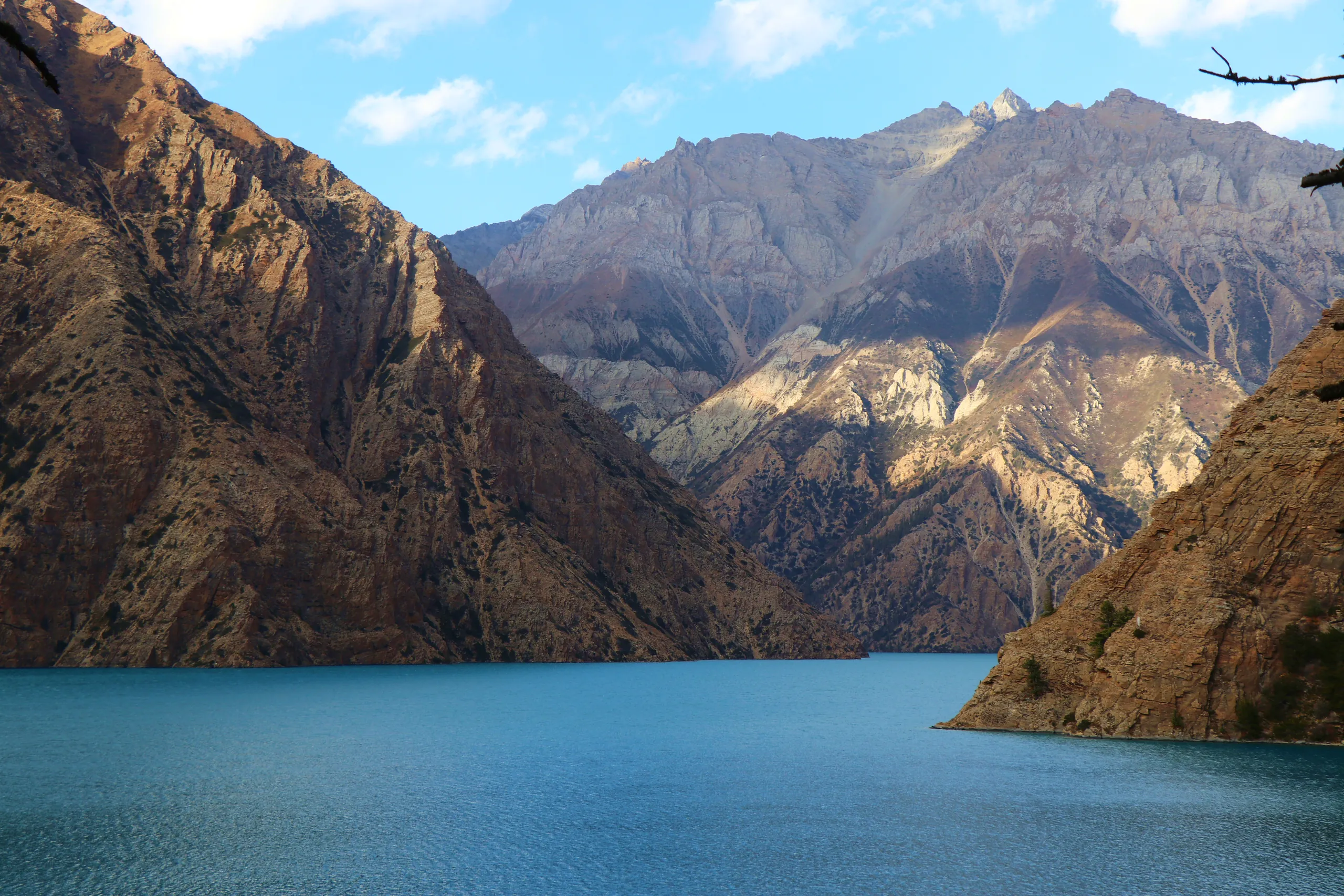 A more subdued and moody portrait of the lake, captured in softer, more diffused light. The water here reads as a deeper, darker blue-teal rather than the electric turquoise seen in other images - as though a cloud has passed overhead or the light has shi