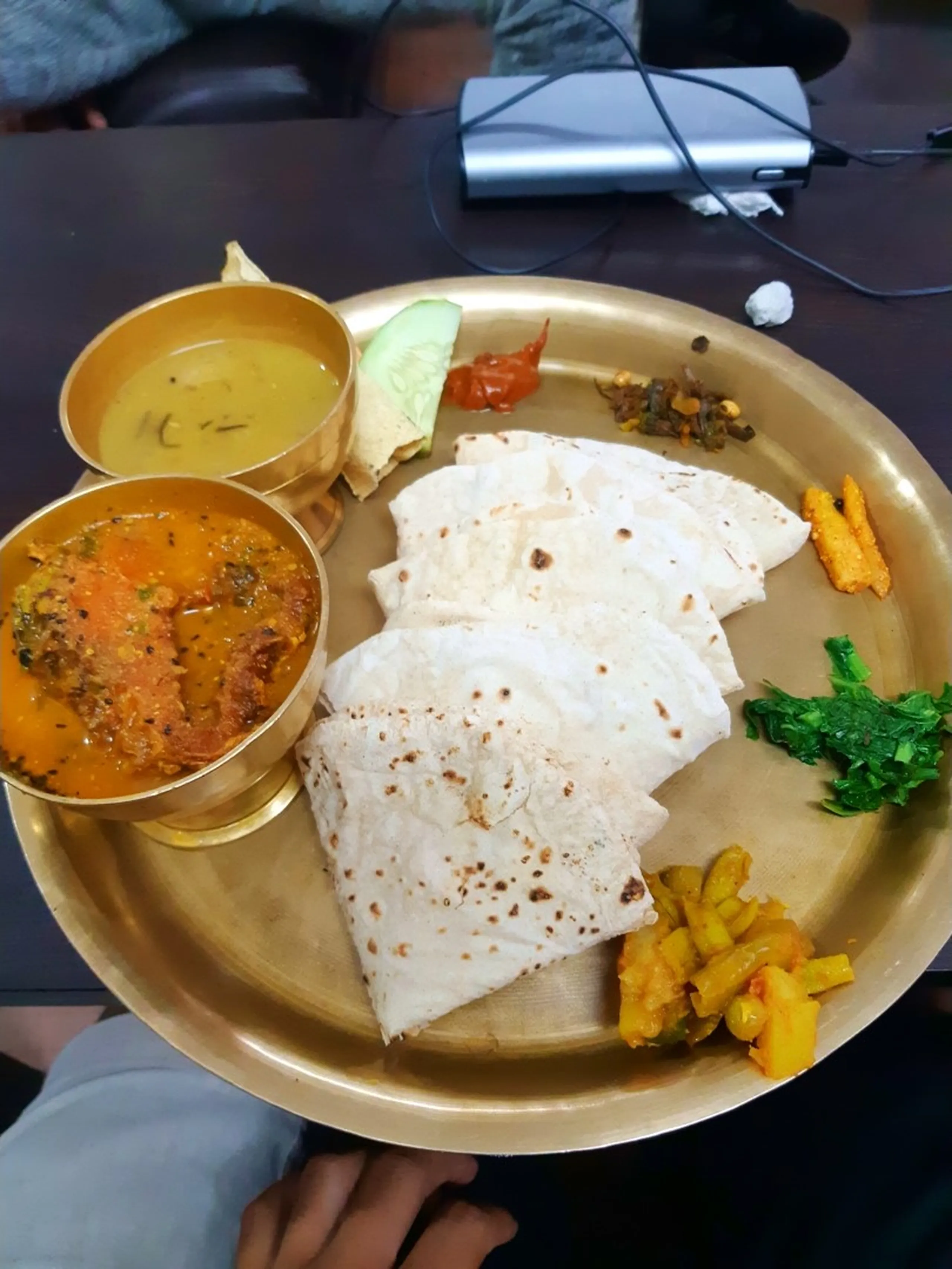 Traditional Nepali thali meal served on a round polished brass plate featuring multiple white roti flatbreads fanned out, two brass bowls of golden dal lentil soup and spiced orange vegetable curry, small portions of green saag, yellow aloo pickle, red tomato chutney, sliced cucumber, and fried snacks - Nepal traditional food dal bhat thali Nepali cuisine trekking meal Kathmandu restaurant